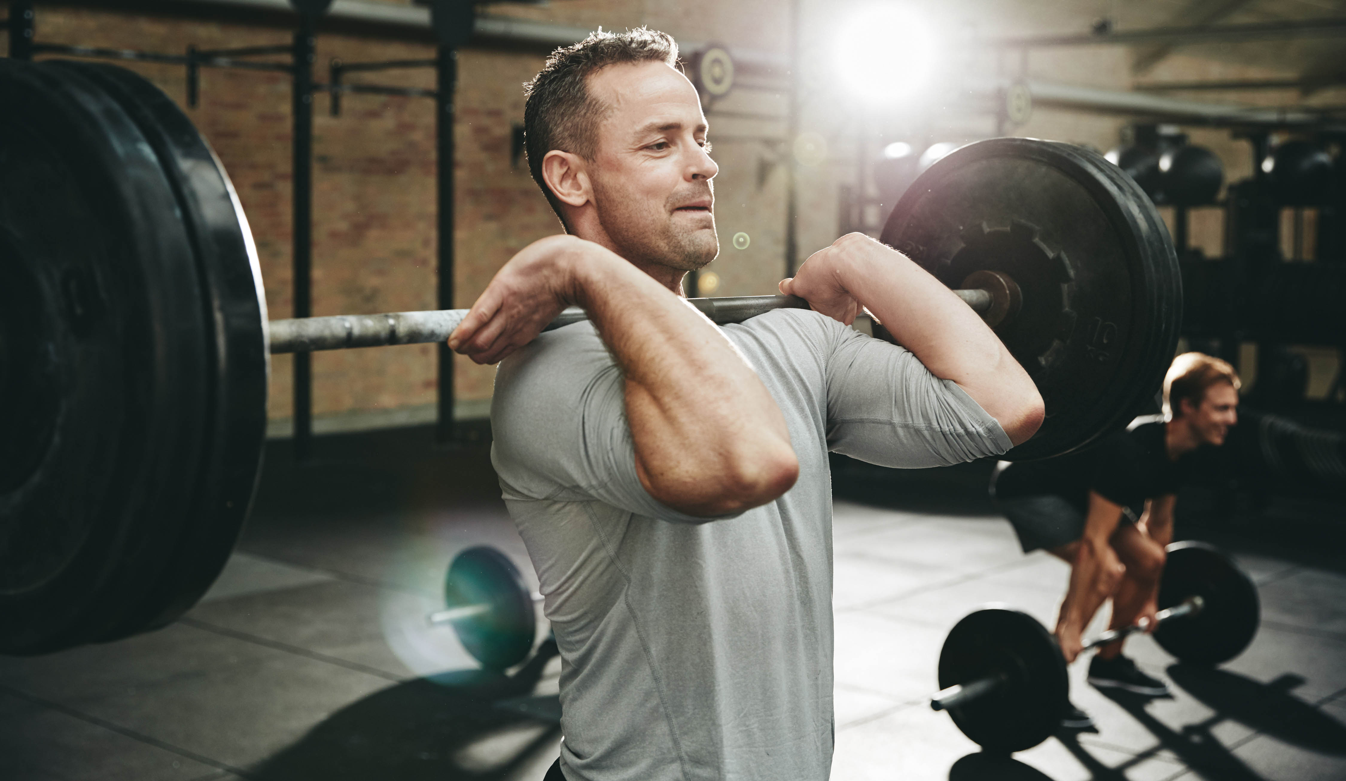 Middle age man standing in the gym with weights and barbell at chest height